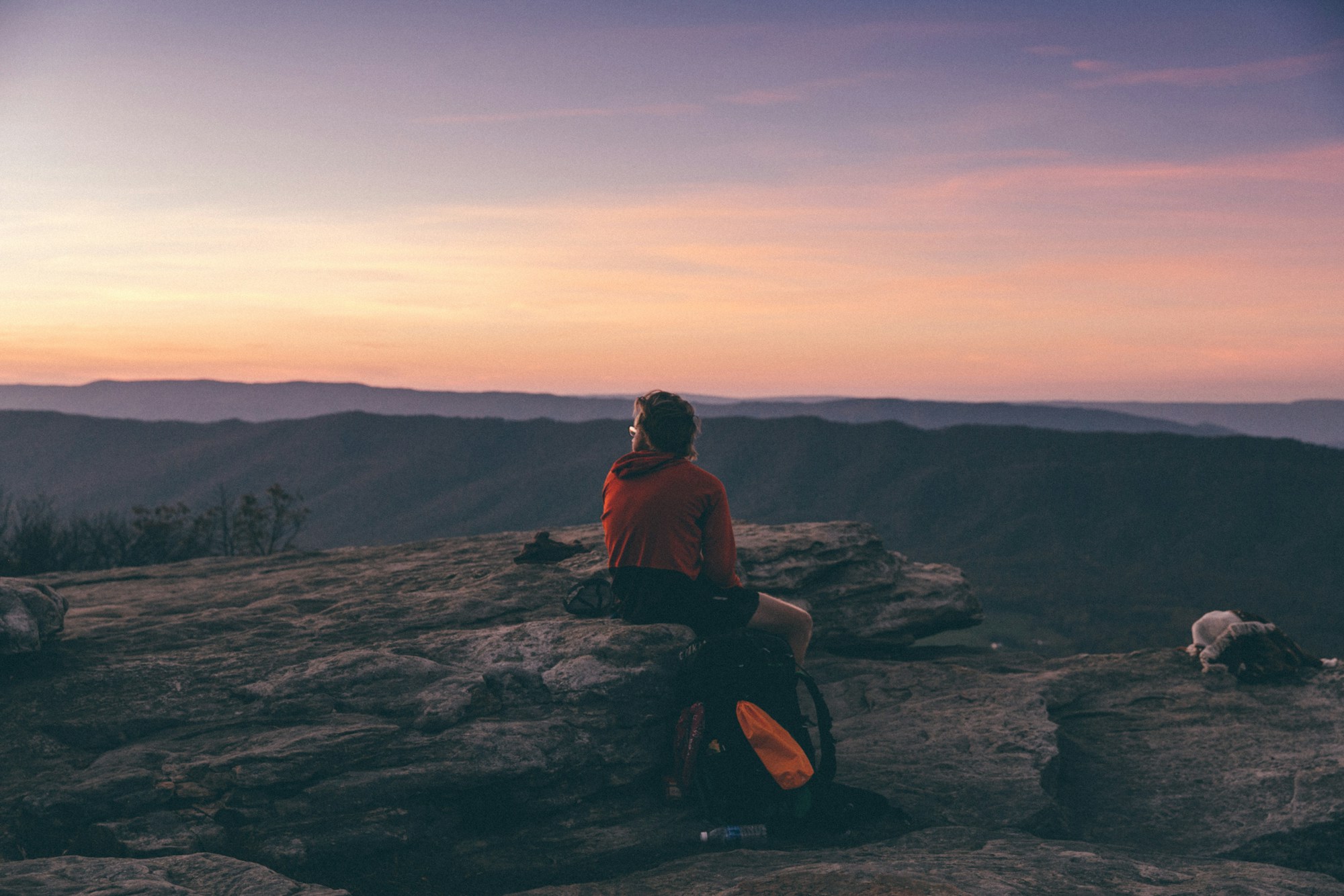 A hiker resting on a boulder at golden hour, overlooking distant mountain ridges